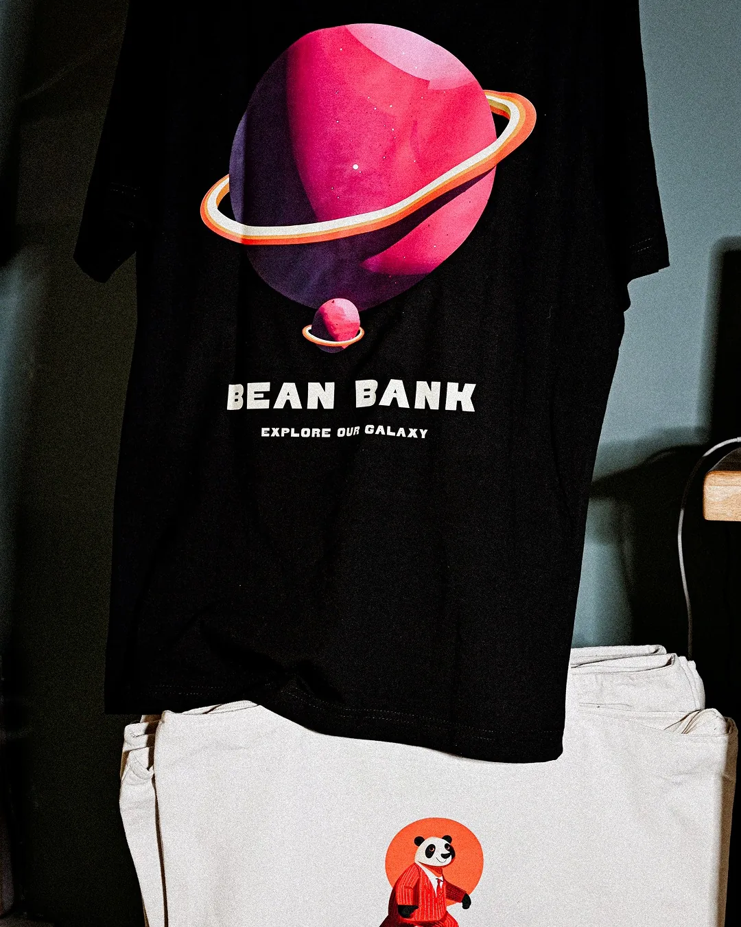 Das T-Shirt mit Galaxie-Druck und die Stofftasche von Bean Bank als Merchandise